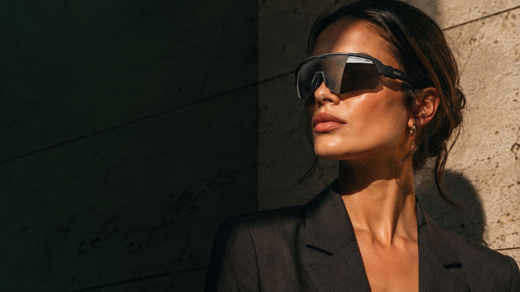 A woman in tailored charcoal wearing the XAGGER Premium Shield against a sunlit travertine wall